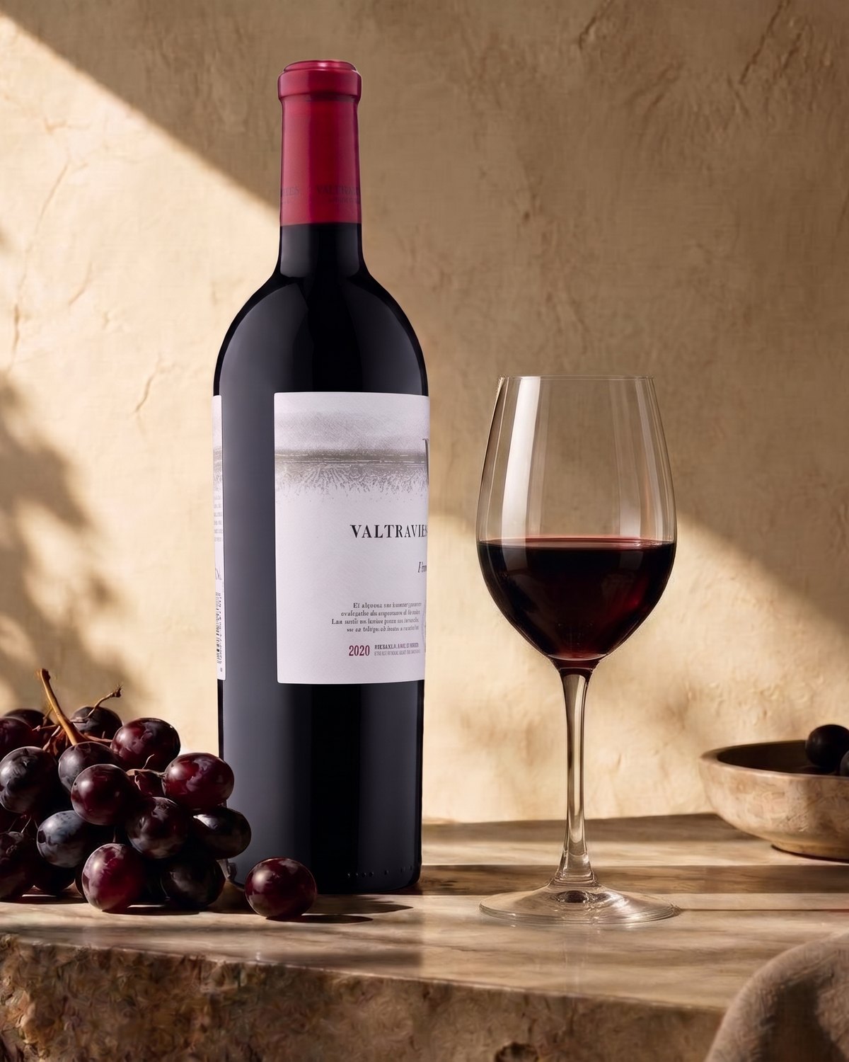 Botella de vino tinto español junto a una copa servida y racimos de uva